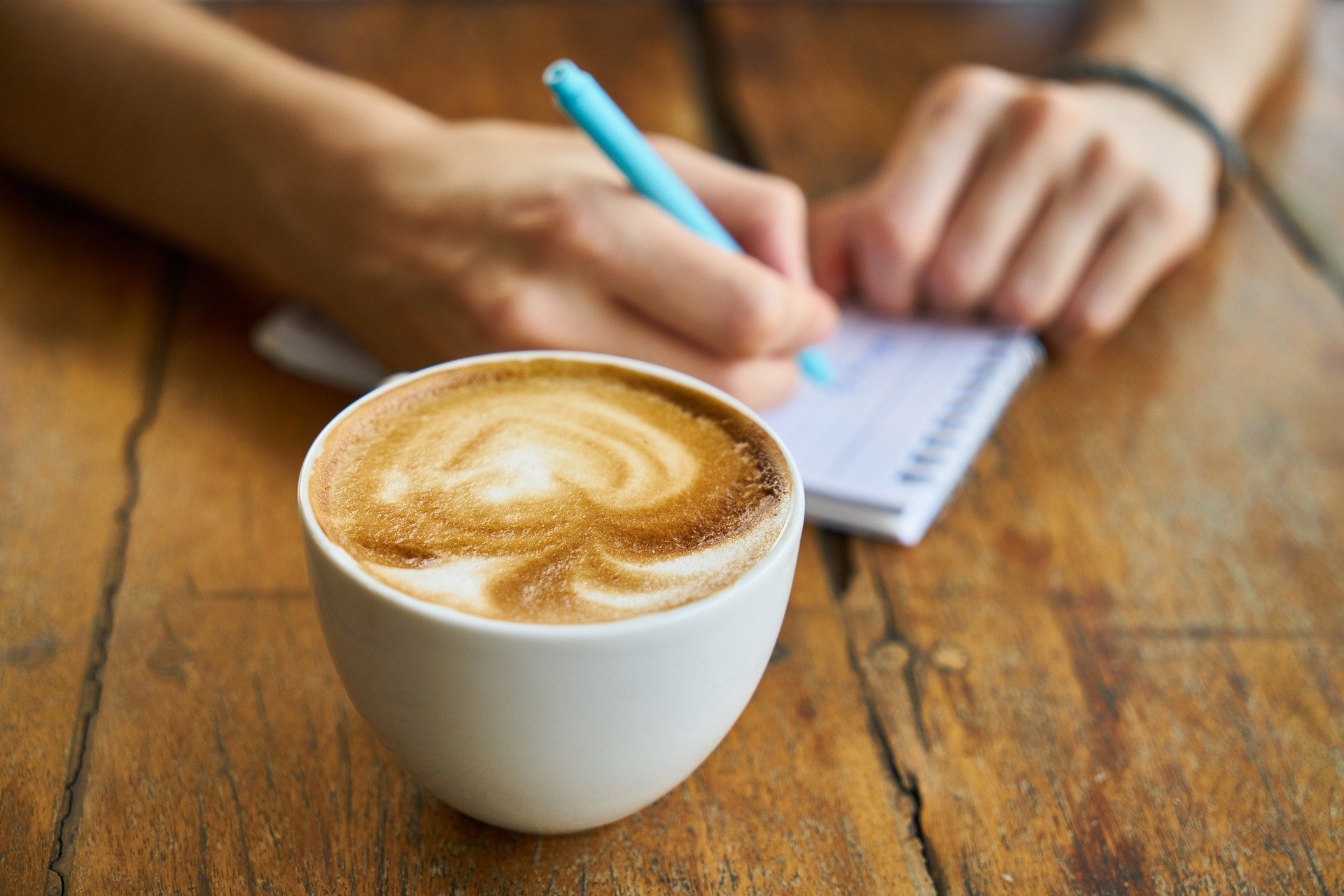 Someone writing in a notebook with a cup of coffee.