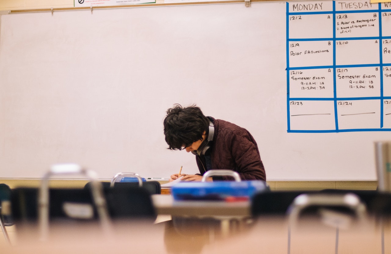 A boy sitting by himself at a desk in a classroom.