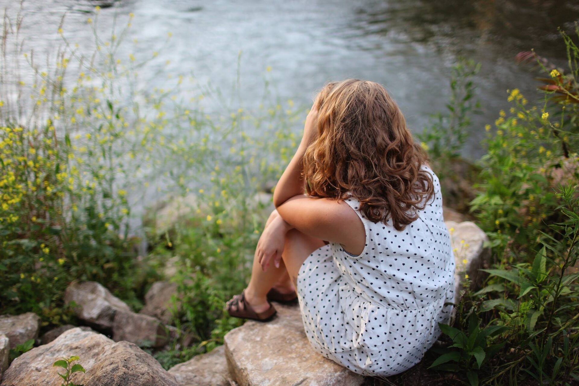 A girl sitting by the water coping with stress.